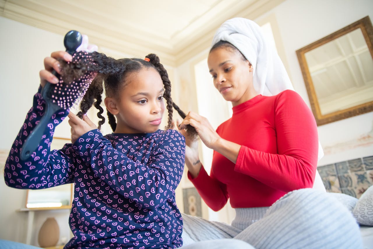 A mother braids her daughters hair at home, emphasizing bonding and ethnic hair care.